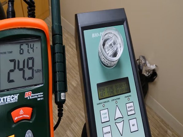 A thermo-hygrometer reading 67.4 degrees Fahrenheit and 24.9 percent relative humidity, beside a spore-trap sampling pump with a cassette fitted